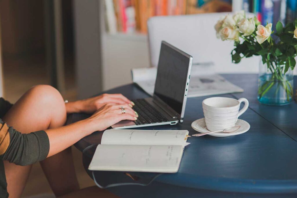 mujer escribiendo un cuento en ordenador con un cuaderno y una taza de café como parte del taller de escritura creativa